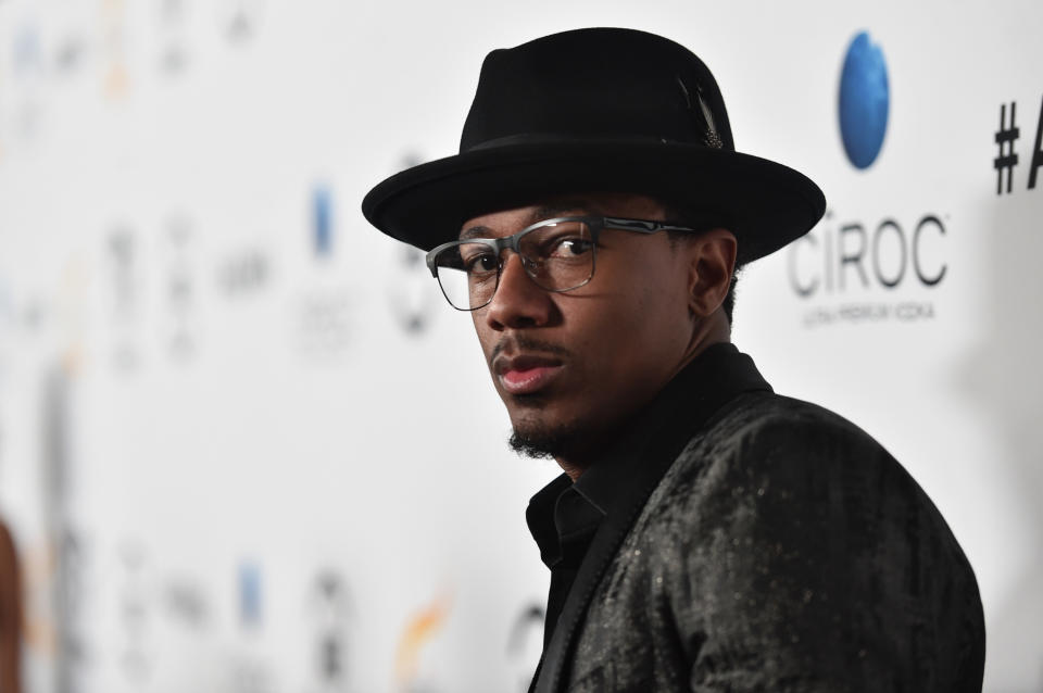 Nick poses for photographers on the red carpet at an event in a fedora and eyeglasses