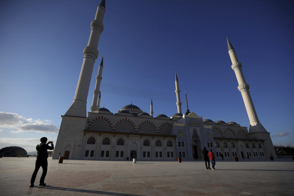 A man, left, takes photos as two others walk at the Camlica mosque in Istanbul, Sunday, March 31, 2019. Turkish citizens have begun casting votes in municipal elections for mayors, local assembly representatives and neighborhood or village administrators that are seen as a barometer of Erdogan's popularity amid a sharp economic downturn. (AP Photo/Emrah Gurel)
