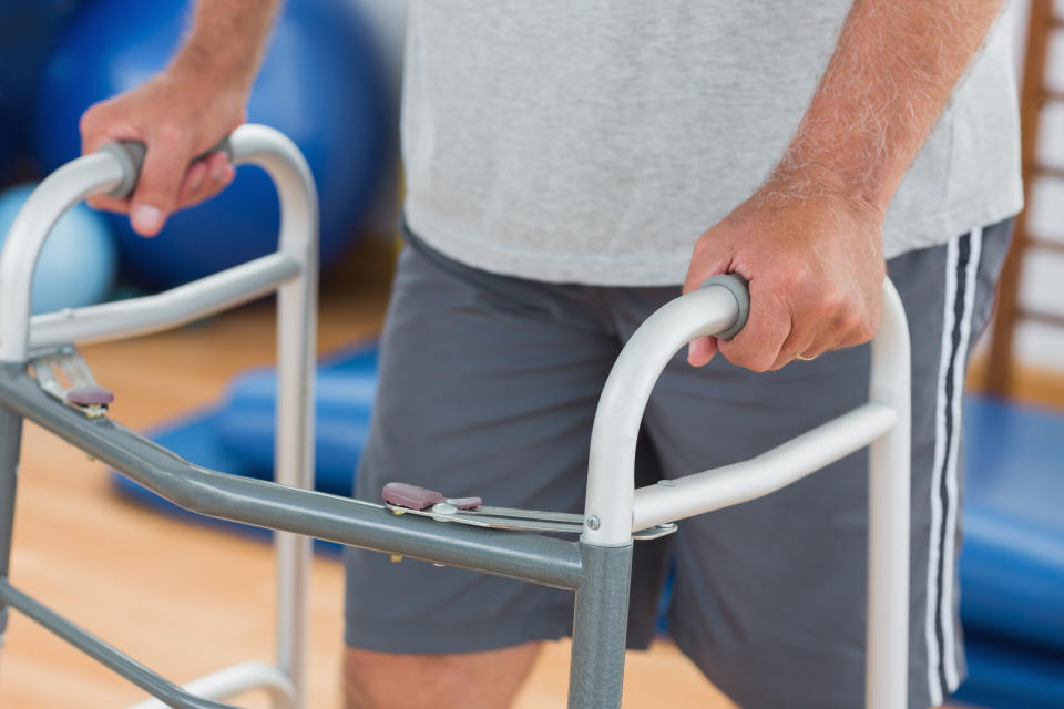 Midsection of male patient walking with zimmer frame at gym