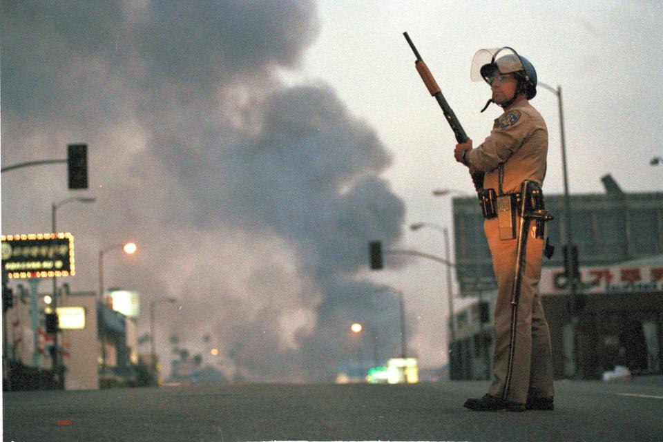 A California Highway Patrol officer stands guard at Ninth Street and Vermont Avenue in Los Angeles as smoke rises from a fire further down the street, April 30, 1992. It was the second day of unrest in Los Angeles following the acquittal of four Los Angeles police officers in the Rodney King beating case.