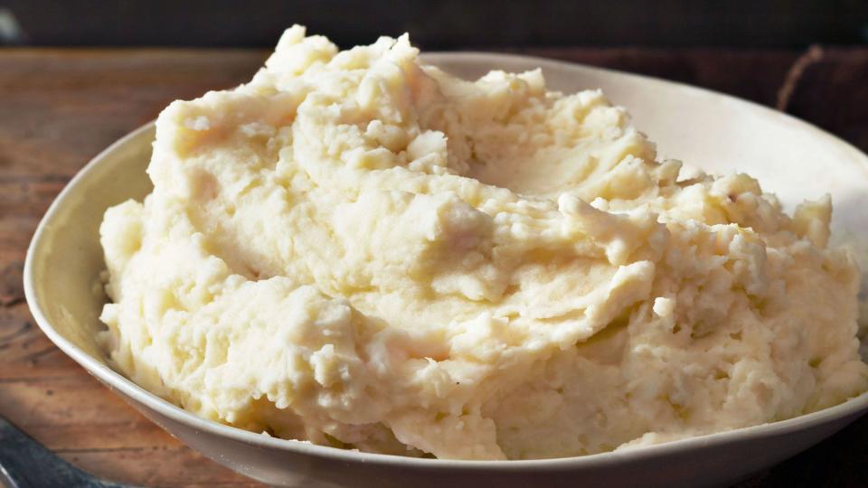 a serving bowl of creamy mashed potatoes with a wooden spoon next to it