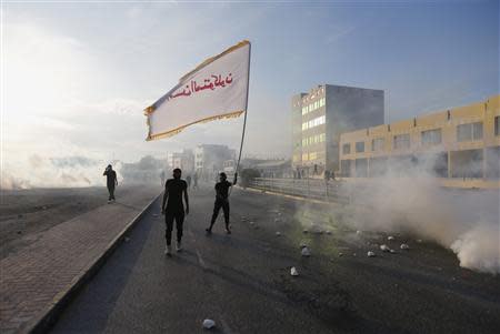 An anti-government protester waves a flag with a religious slogan on it as he confronts riot police amidst teargas, during clashes after the revisit to the grave of detainee Jaffar Mohammed Jaffar, in the village of Daih west of Manama, March 3, 2014. REUTERS/Hamad I Mohammed