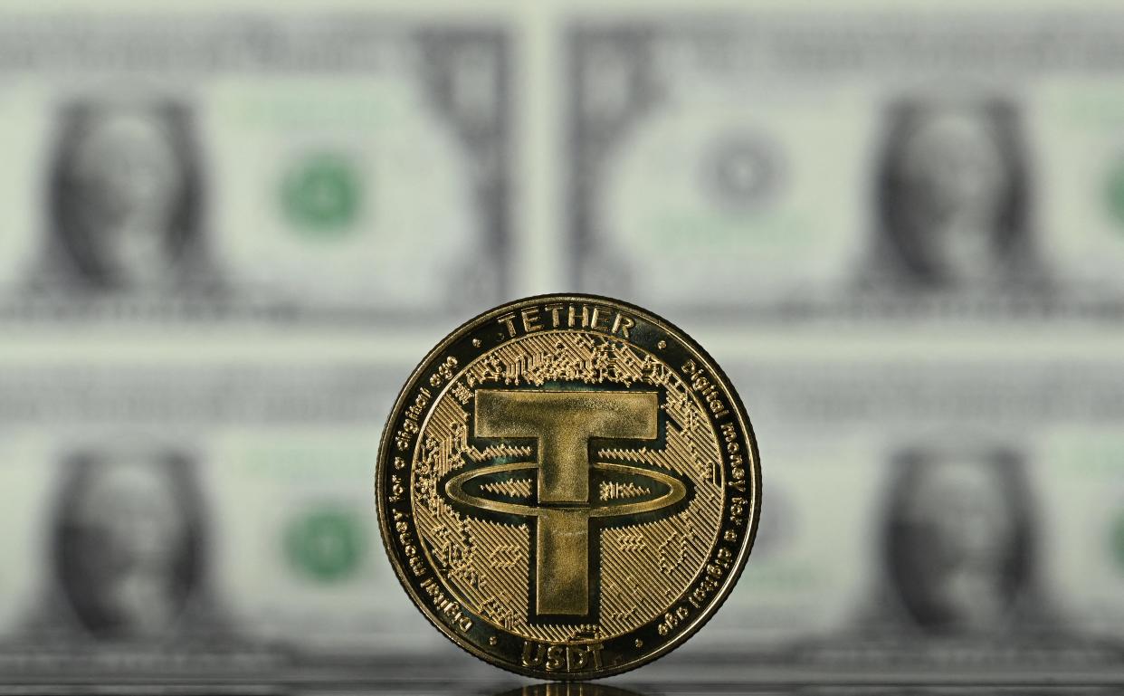 An illustration picture taken in London on May 8, 2022, shows a gold plated souvenir cryptocurrency Tether (USDT) coin arranged beside a screen displaying US dollar notes. - Tether (USDT) is an Ethereum token known as a stablecoin that is pegged to the value of the US dollar, and is currently the largest stablecoin with a market value of USD 83 billion dollars. (Photo by Justin TALLIS / AFP) (Photo by JUSTIN TALLIS/AFP via Getty Images)