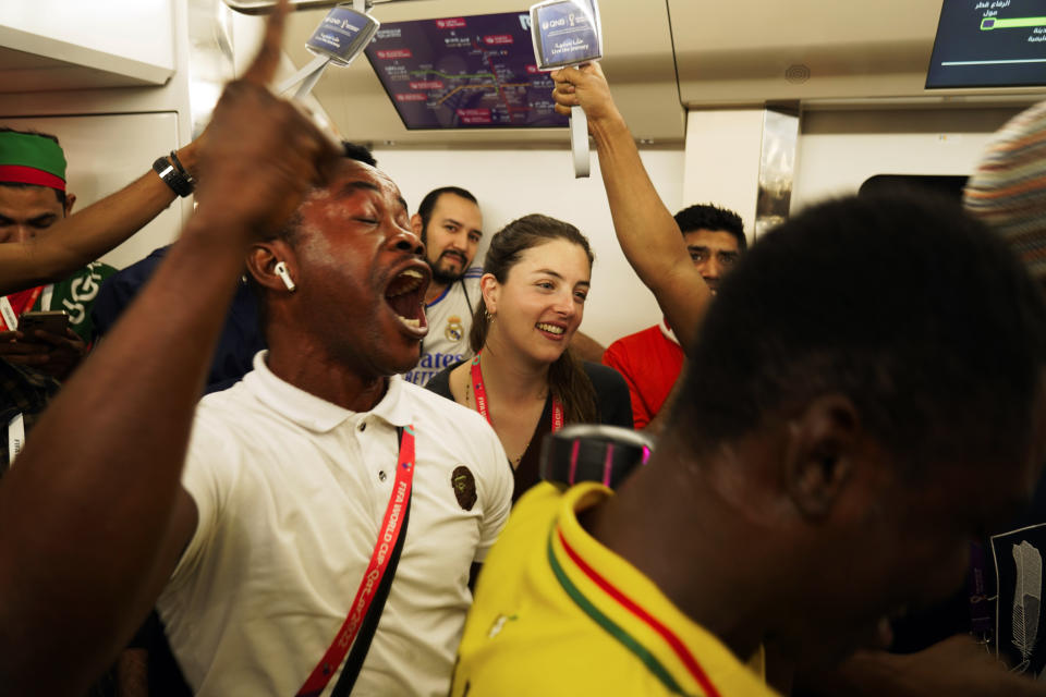 Associated Press correspondent Isabel DeBre, center, smiles as Ghana fans celebrate their win in the Doha Metro in Doha, Qatar, Monday, Nov. 28, 2022. With Qatar's World Cup the most compact tournament in the competition's history, DeBre set out to see four matches in one day. (AP Photo/Jon Gambrell)