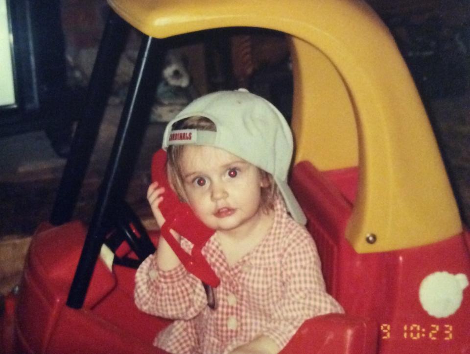 Sam Bailey wearing her signature look of a backwards hat while on the phone, presumably conducting an interview. The hat is a Saint Louis Cardinals cap, the baseball team she grew up watching.