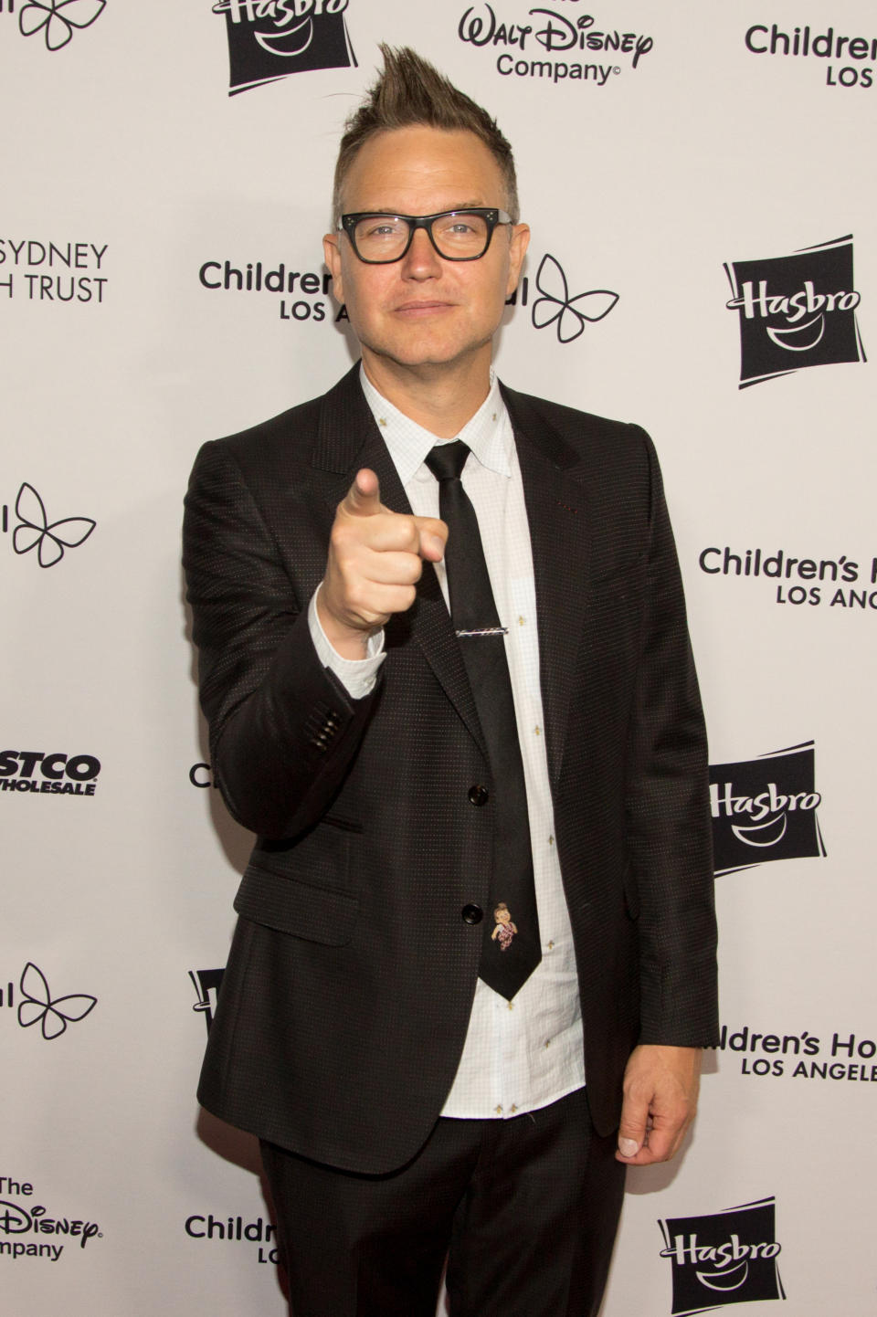 Man in a black suit with a patterned tie giving a thumbs-up at a charity event