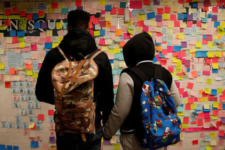 People holds hands looking at post-election Post-it notes pasted along a tiled walk at Union Square subway station in New York U.S., November 14, 2016. REUTERS/Shannon Stapleton/File Photo