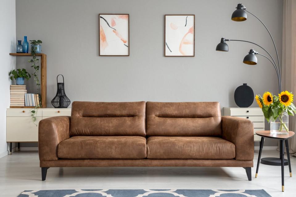 Leather sofa next to table with sunflowers in grey living room interior with posters