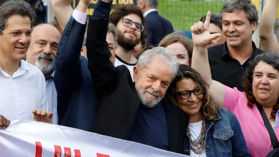 Lula, com os punhos erguidos em sinal de vitória, abraça uma mulher jovem de cabelos castanhos com luzes loiras