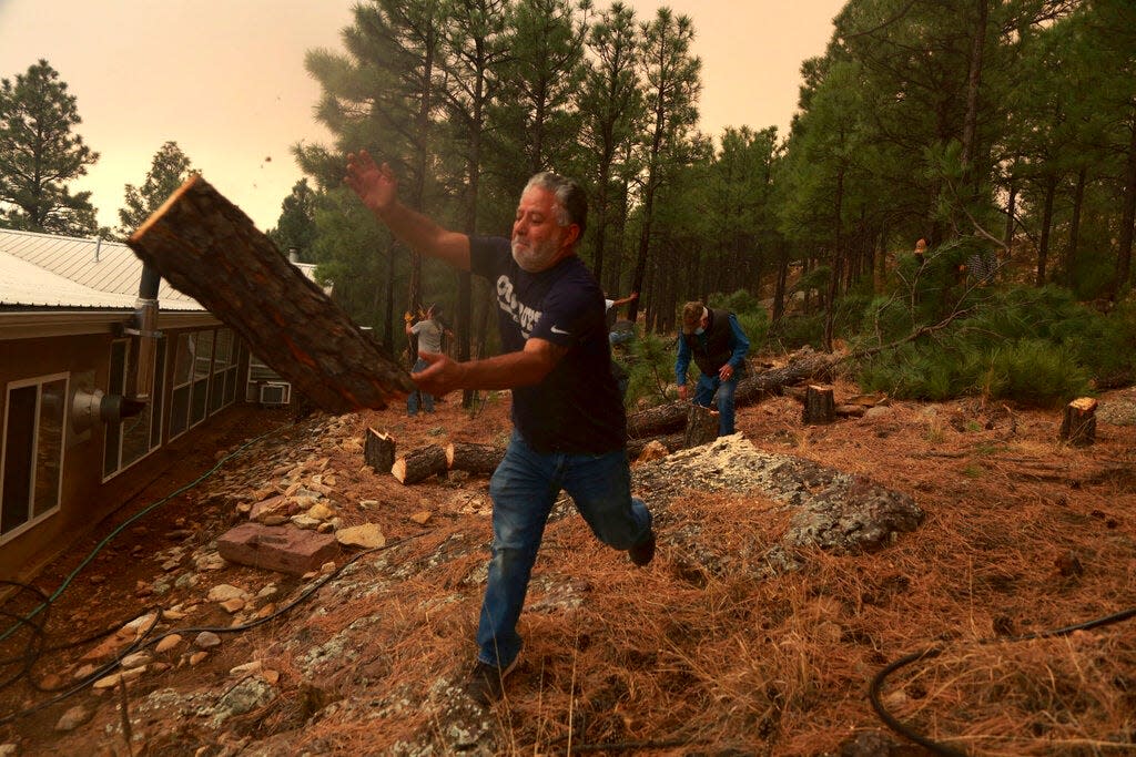 Chris Castillo throws a freshly-cut log as he and his cousins clear a wireline along a family member's home in Las Vegas, N.M., Monday, May 2, 2022. Wind-whipped flames are marching across more of New Mexico's tinder-dry mountainsides, forcing the evacuation of area residents and dozens of patients from the state's psychiatric hospital as firefighters scramble to keep new wildfires from growing.