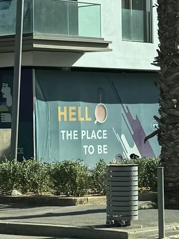 Text on a building reads "Hell the place to be," it intends to say "Hello" but they've used a coffee mug as the O and it really doesn't appear to be part of the actual text at all