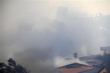 Firefighters work to put out a fire at the location where a forest fire burned several neighbourhoods in the hills in Valparaiso city, northwest of Santiago, April 13, 2014. REUTERS/Cristobal Saavedra