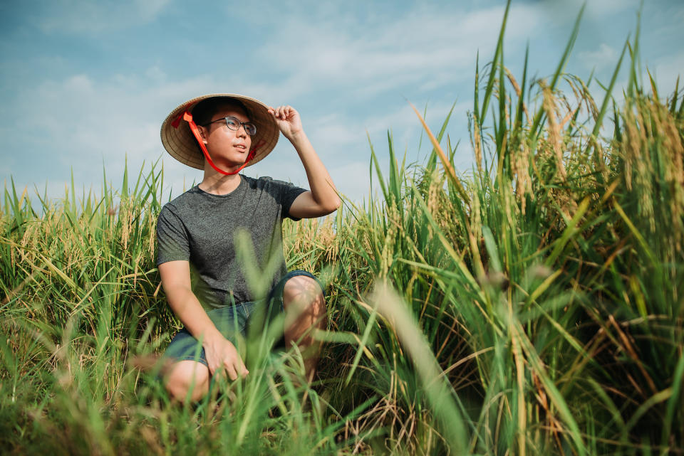 A man with a rattan hat sitting among green grass in a field.