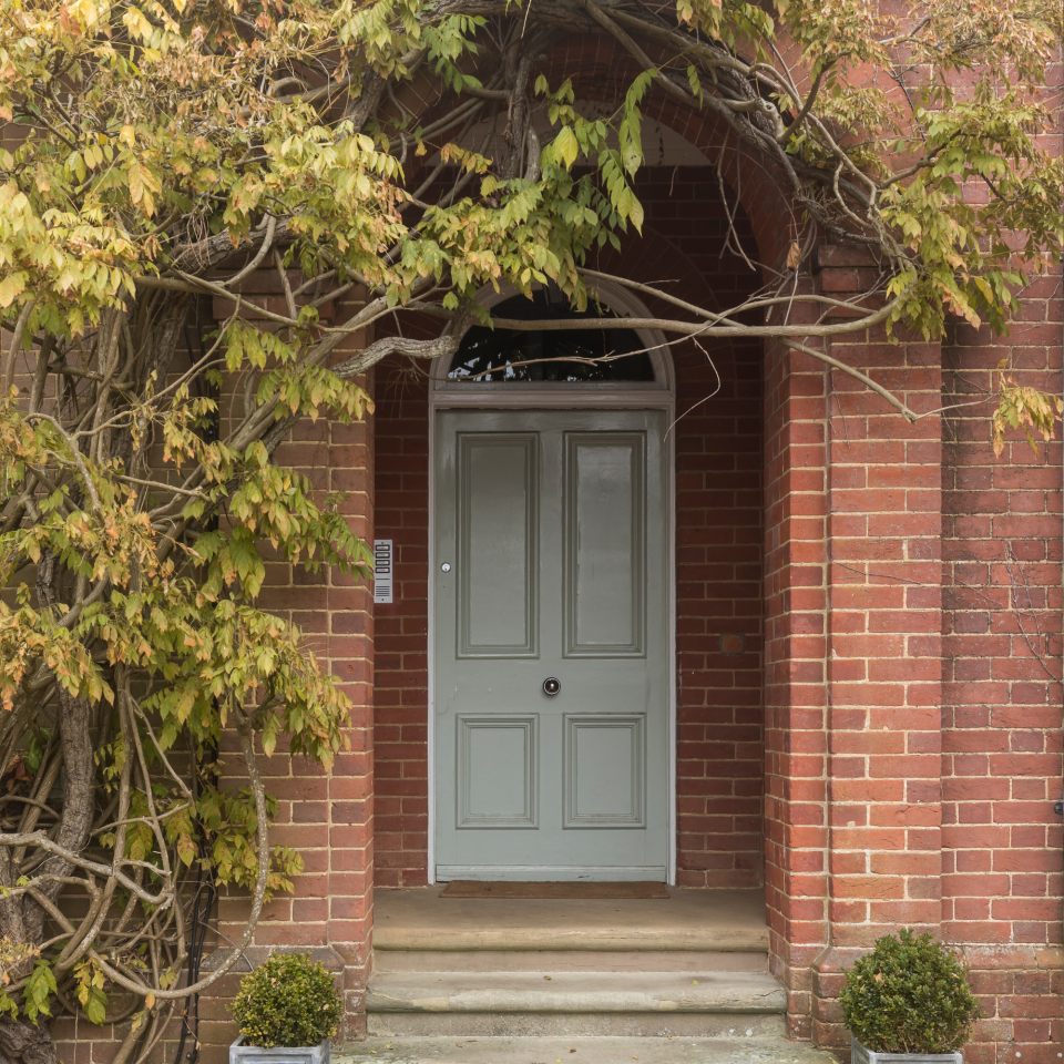 Front door of a red brick house, with climbing plants on the walls. Renovated flat in an Edwardian villa in Surrey, home of Lisa James.