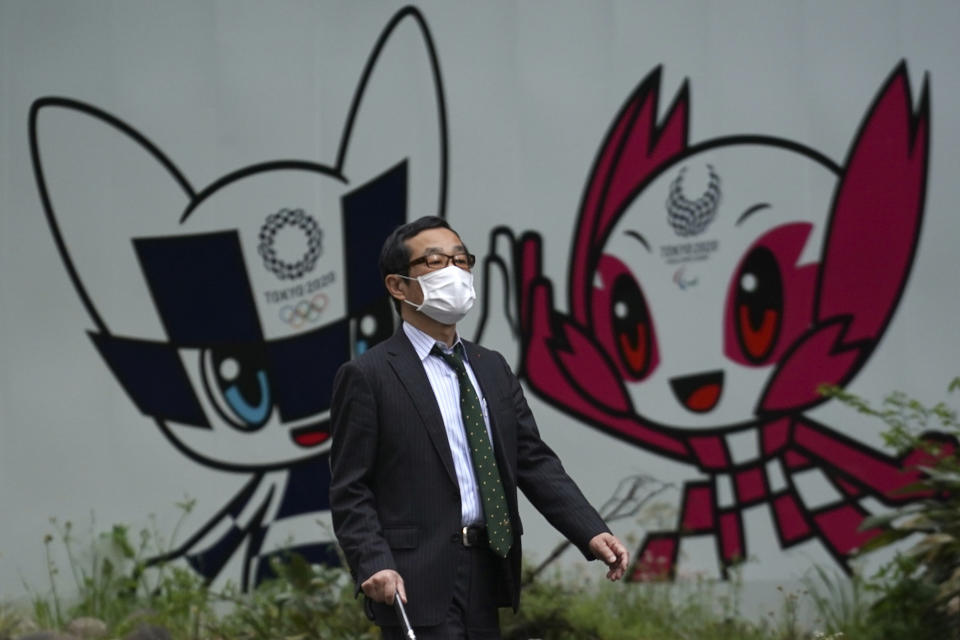 FILE - In this April 28, 2020, file photo, a man with a face mask against the spread of the new coronavirus walks in front of Miraitowa and Someity, mascots for the Tokyo 2020 Olympics and Paralympics at a park in Tokyo. The postponed Tokyo Olympics have again reached the one-year-to-go mark. But the celebration is small this time with more questions than answers about how the Olympics can happen in the middle of a pandemic. That was before COVID-19 postponed the Olympics and pushed back the opening to July 23, 2021. (AP Photo/Eugene Hoshiko, File)