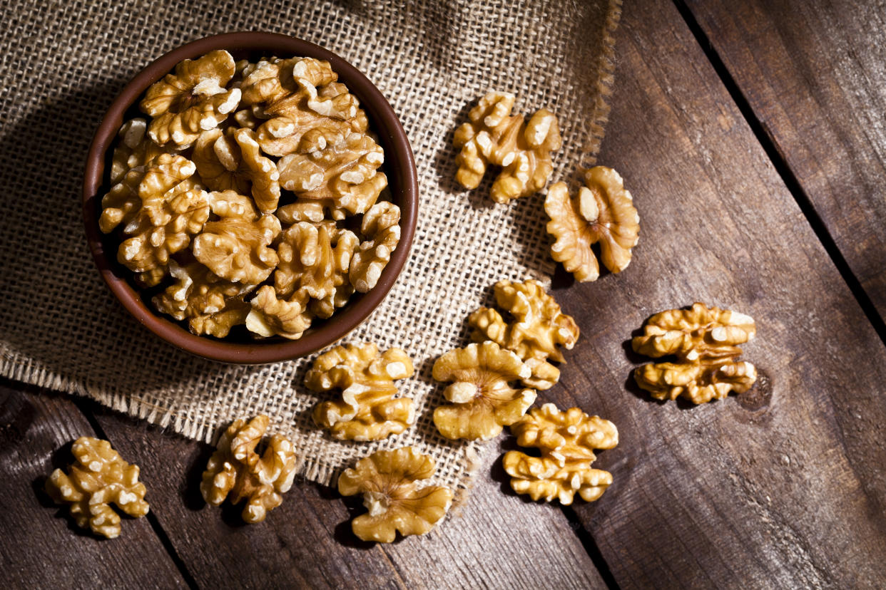 Top view of a brown bowl filled with organic walnuts shot on rustic wood table. Some almonds are out of the bowl on a burlap. Predominant color is brown. DSRL studio photo taken with Canon EOS 5D Mk II and Canon EF 100mm f/2.8L Macro IS USM