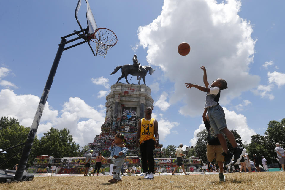 Isaiah Bowen, right, takes a shot as his dad, Garth Bowen, center, looks on at a basketball hoop in front of the statue of Confederate General Robert E. Lee on Monument Avenue Sunday June 21, 2020, in Richmond, Va. A judge extended an injunction delaying the removal of the statue by the state. The statue had become a focal point for the Black Lives Matter movement in Richmond. (AP Photo/Steve Helber)