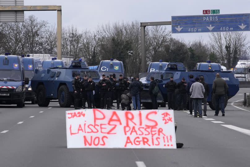 A placard reads "Paris, let our farmers get through" as gendarmes with armored vehicles face farmers and their tractors blocking a highway Jan. 31, 2024 