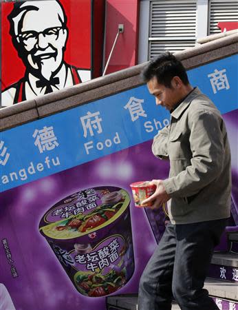 A man holding an instant cup noodle pack walks past a logo of KFC in Beijing October 23, 2013. REUTERS/Kim Kyung-Hoon