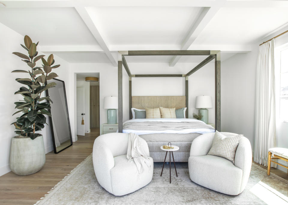 White bedroom with four poster bed and two curved armchairs