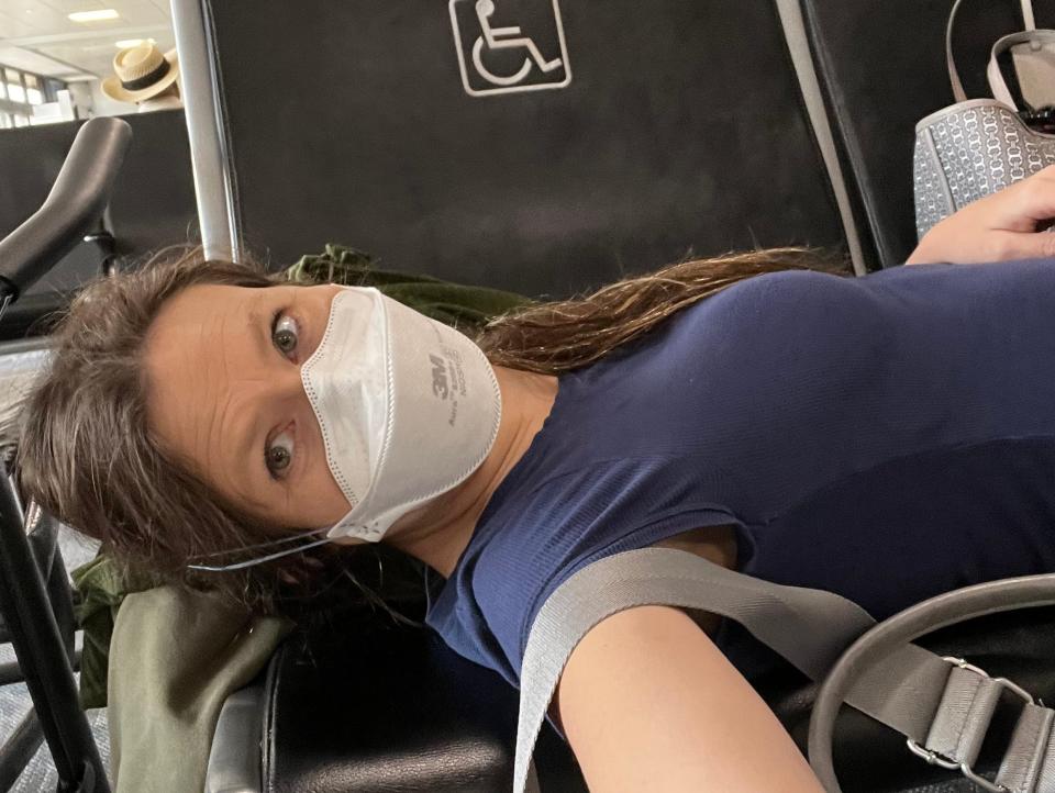 Samantha Brandon lying down on chairs at the airport wearing a mask