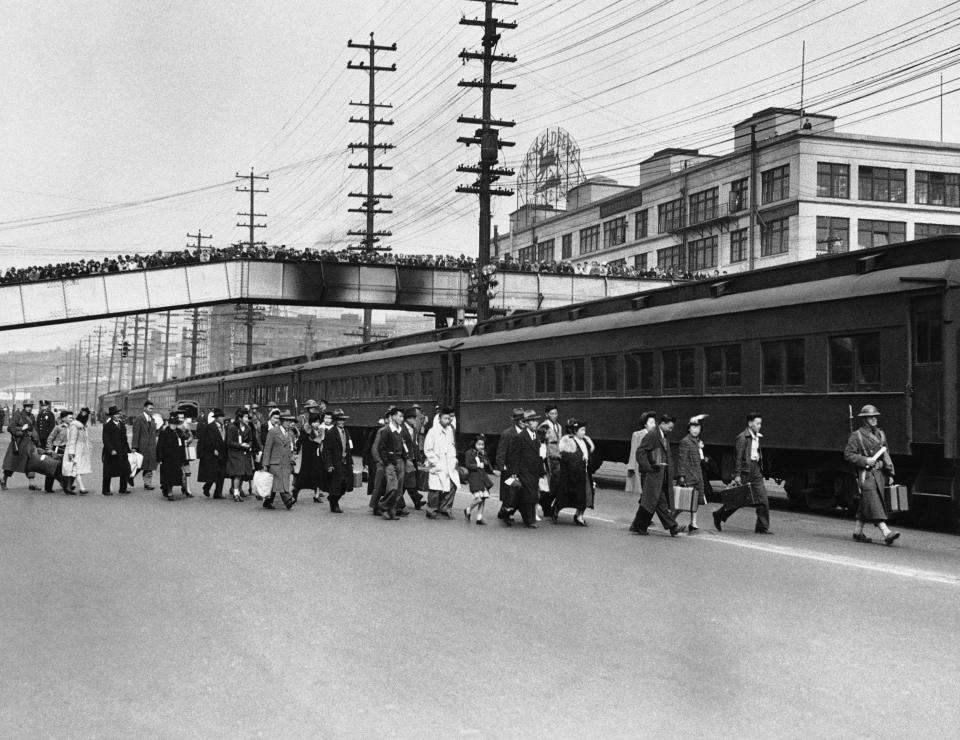 FILE - In this March 30, 1942, file photo, Seattle crowds jam an overhead walk to witness mass evacuation of Japanese from Bainbridge Island, Washington. Somewhat bewildered, but not protesting, some 200 Japanese men, women and children were taken by ferry, bus and train to California internment camps. Evacuation was carried out by the army. (AP Photo, File)