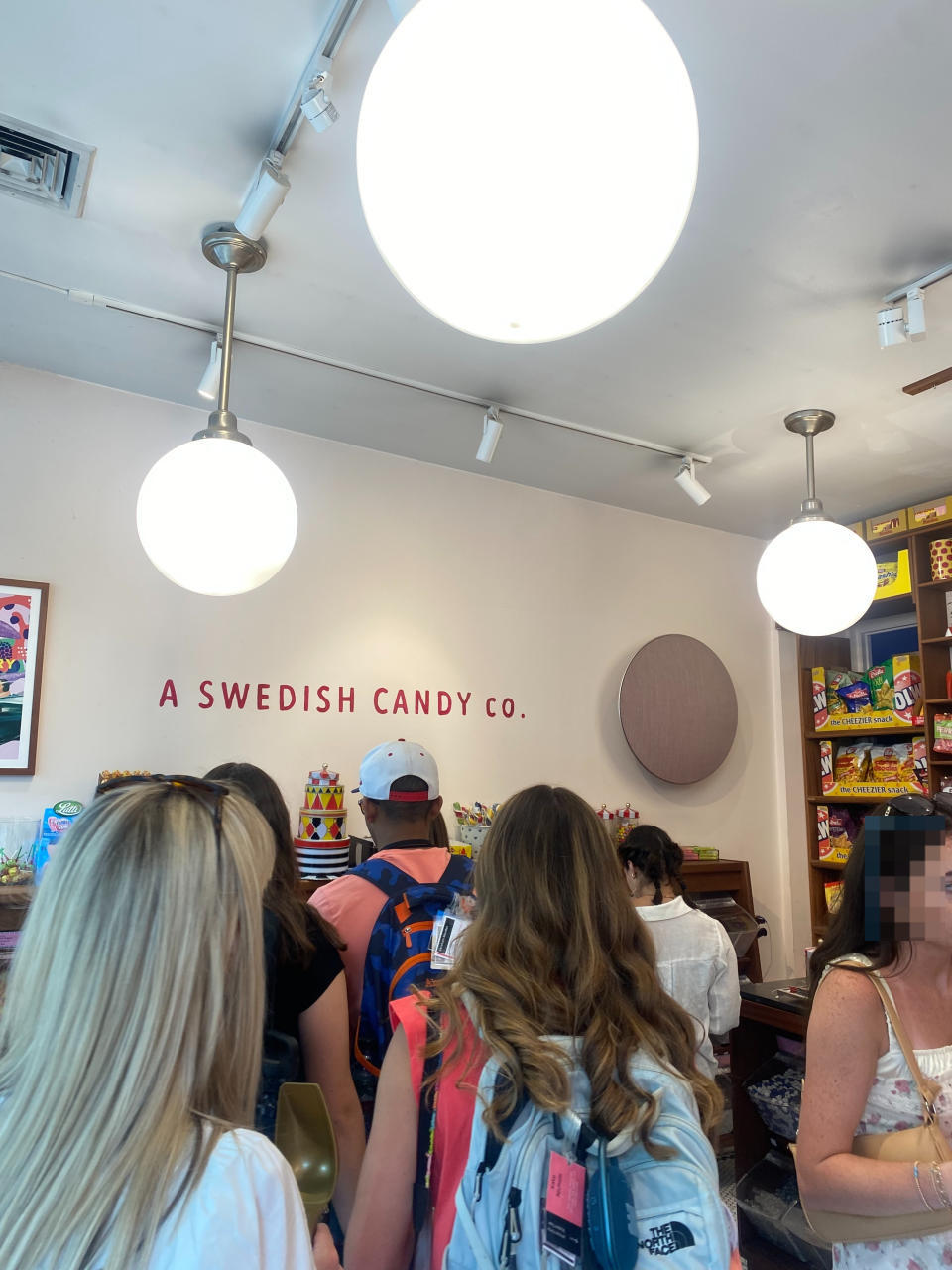 People wait in line inside BonBon, with shelves of colorful candy visible in the background
