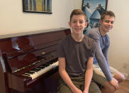 This Nov. 20, 2020 photo released by Andrea Fage shows brothers Rafael Fage, 16, background, ad Noah Fage, 14 posing at the piano at their home in Harrison, N.Y. During the pandemic lockdown, private piano lessons for boys stopped. They researched movie soundtracks and learned the score on their own with the assistance of sites like YouTube. (Andrea Fage via AP)