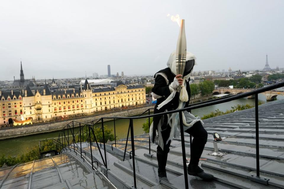 A mysterious torchbearer carries the Olympic flame over a building along the Seine River (Getty Images)