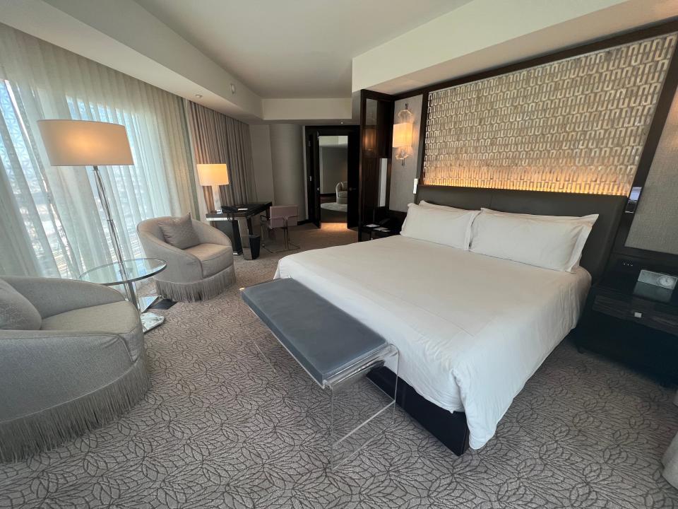 A hotel bedroom with a bed, bench, chairs, and desk.