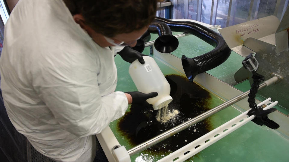 In this Dec. 9, 2016 photo, courtesy of Pacific Northwest National Laboratory, PNNL microbiologist Robert Jeters sprinkles PNNL's chemically modified sawdust onto a small oil spill inside the Arctic simulation lab, where researchers mimic extreme freezing conditions and make icy slush that is similar to what is found on the surface of the Arctic Sea during a demonstration of sawdust oil recovery material research at the PNNL in Richland, Wash. (Pacific Northwest National Laboratory via AP)