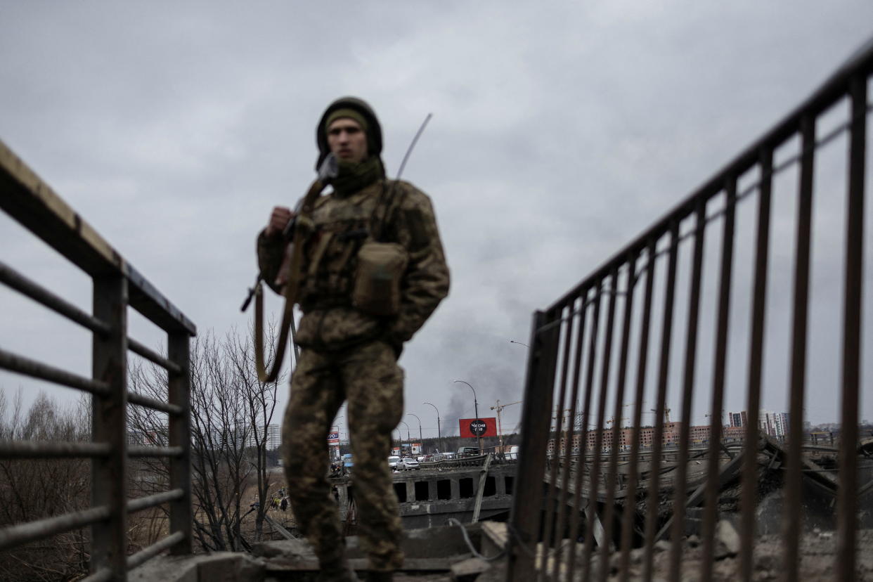 Smoke rises as a service member of the Ukrainian armed forces stands by the only escape route used by locals to evacuate from the town of Irpin, after days of heavy shelling, while Russian troops advance towards the capital, in Irpin, near Kyiv, Ukraine March 7, 2022. (Reuters)