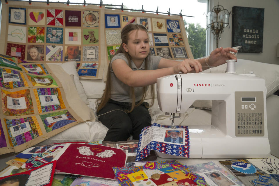 High school freshman Madeleine Fugate works surrounded by several quilts that are part of the COVID Memorial Quilt to honor and remember those who died of COVID-19, at her home in Los Angeles, Wednesday, Oct. 27, 2021. Fugate's memorial quilt started out in May 2020 as a seventh grade class project. Inspired by the AIDS Memorial Quilt, which her mother worked on in the 1980s, the then-13-year-old encouraged families in her native Los Angeles to send her fabric squares representing their lost loved ones that she'd stitch together. (AP Photo/Damian Dovarganes)