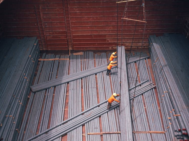 Three workers loading large steel rods