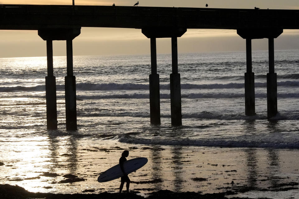 A surfer passes the pilings of the Ocean Beach pier Tuesday, Jan. 30, 2024, in San Diego. Rising seas, frequent storms take toll on California's iconic piers, threatening beach landmarks. (AP Photo/Gregory Bull)