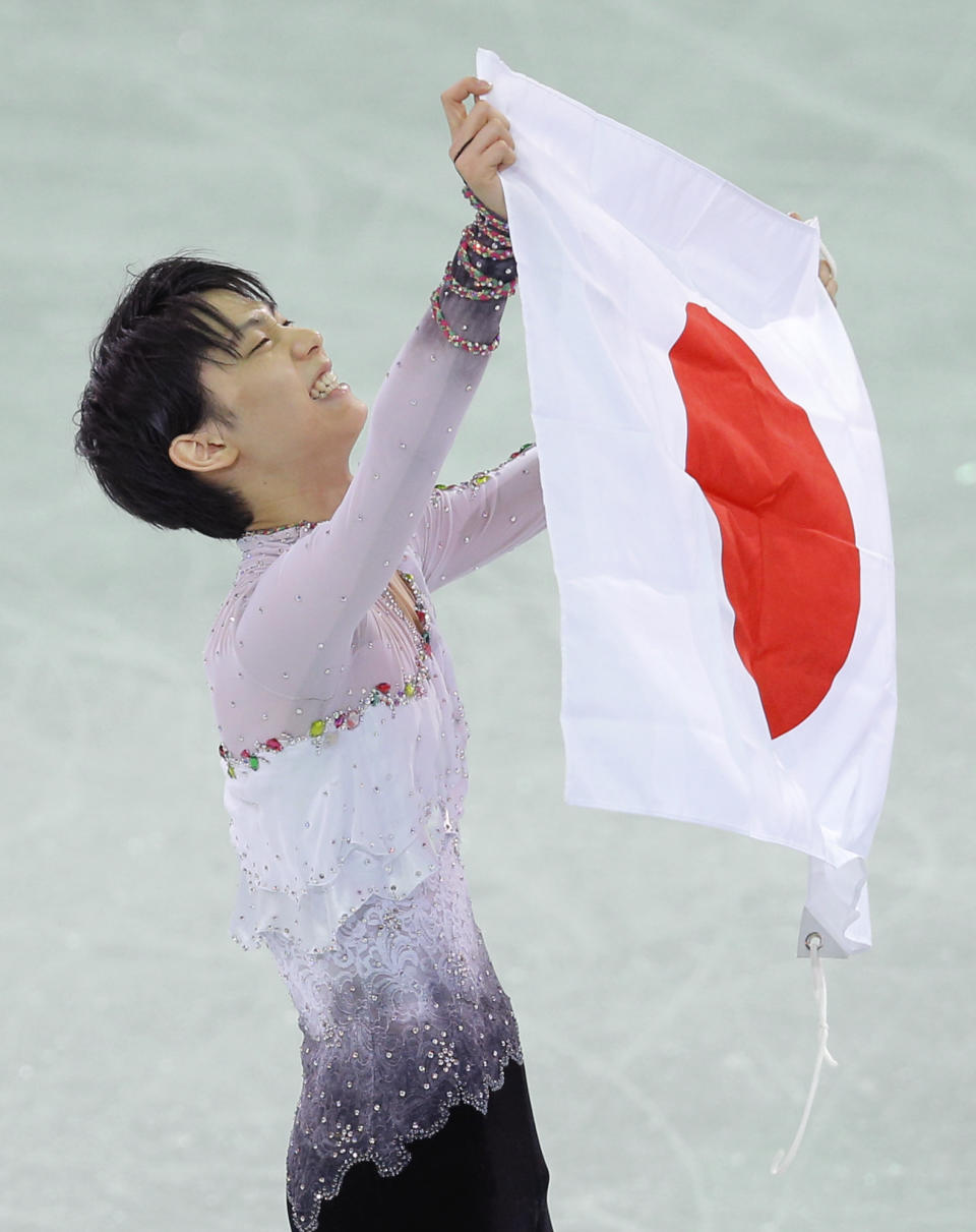 Yuzuru Hanyu of Japan poses with the national flag after he placed first in the men's free skate figure skating final following the flower ceremony at the Iceberg Skating Palace during the 2014 Winter Olympics, Friday, Feb. 14, 2014, in Sochi, Russia. (AP Photo/Vadim Ghirda)