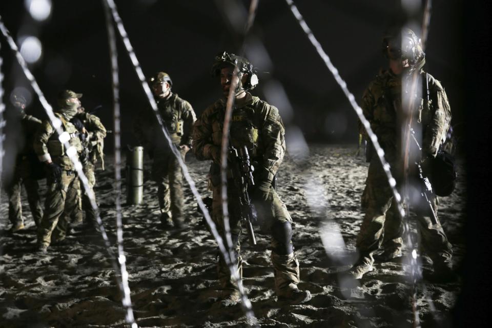 Agentes de la Patrulla Fronteriza de Estados Unidos permanecen de guardia en el lado estadounidense de la frontera con México, vistos a través del alambre de concertina desde Tijuana, México, donde la línea fronteriza se encuentra con el Océano Pacífico, el jueves 15 de noviembre de 2018. (AP Foto/Marco Ugarte)