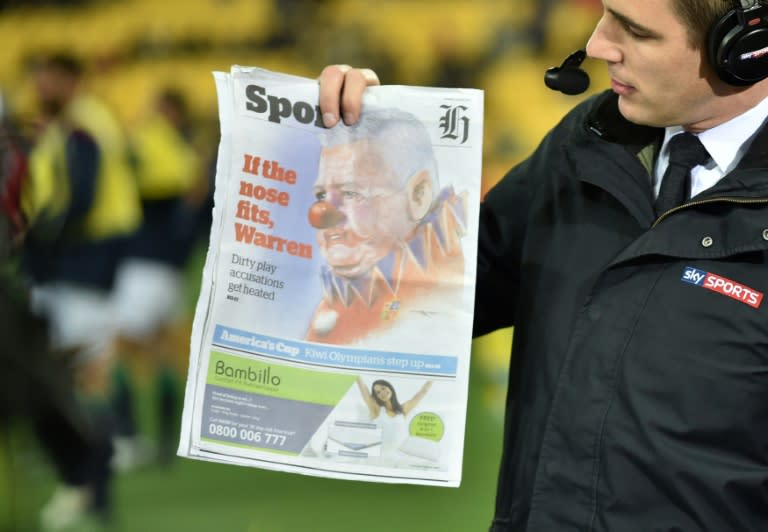 A TV host holds up a newspaper with an image of British and Irish Lions coach Warren Gatland depicted as a clown before their match against the Wellington Hurricanes at Westpac Stadium in Wellington on June 27, 2017