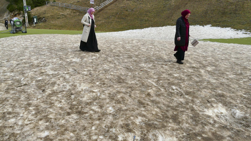 Women walk on a patch of melting artificial snow in Vlasic, a ski resort affected by unusual warm weather in Bosnia, Tuesday, Jan. 3, 2023. The exceptional wintertime warmth is affecting ski resorts across Bosnia, prompting tourism authorities in parts of the country to consider declaring a state of natural emergency. (AP Photo/Almir Alic)