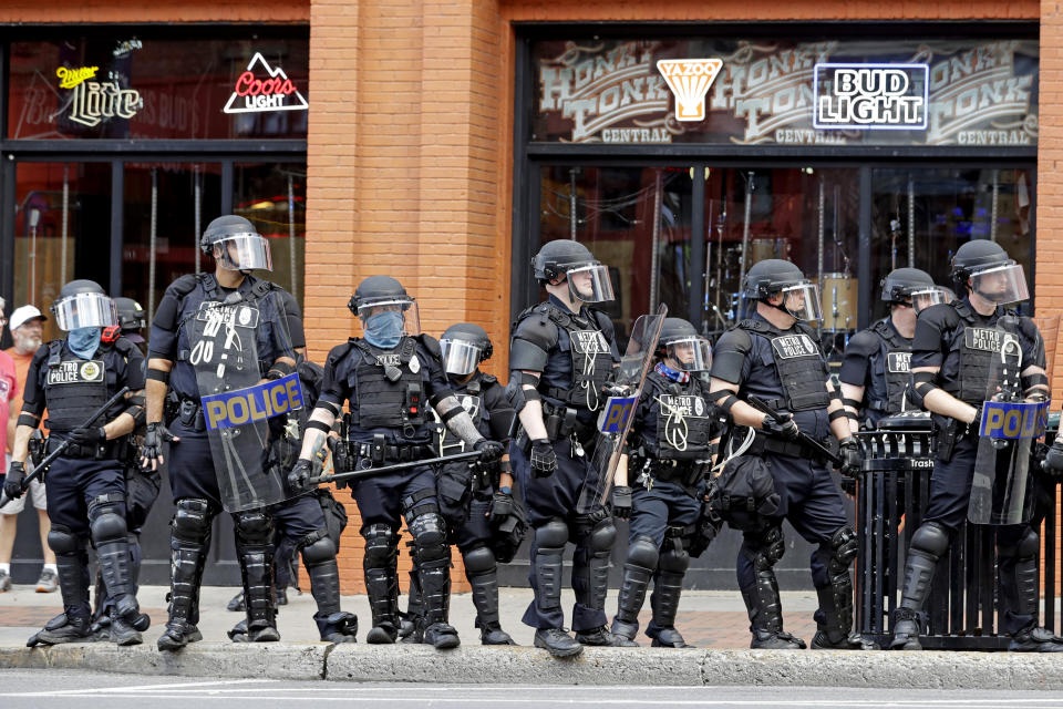FILE — In this June 4, 2020, file photo, Metro Police officers watch as marchers in a protest pass through downtown Nashville, Tenn. After years of delay, Nashville is committing to equipping its police force with body cameras and in-car cameras. (AP Photo/Mark Humphrey, File)