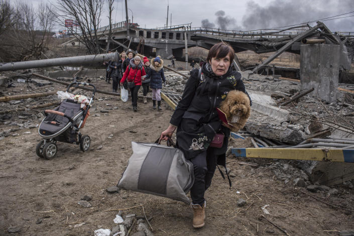 A woman carrying a bag and a dog, followed by others, flees Irpin, Ukraine.