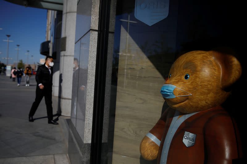 A man wearing a face mask walks near of a bear doll, following an outbreak of the coronavirus disease (COVID-19), in Beijing, China