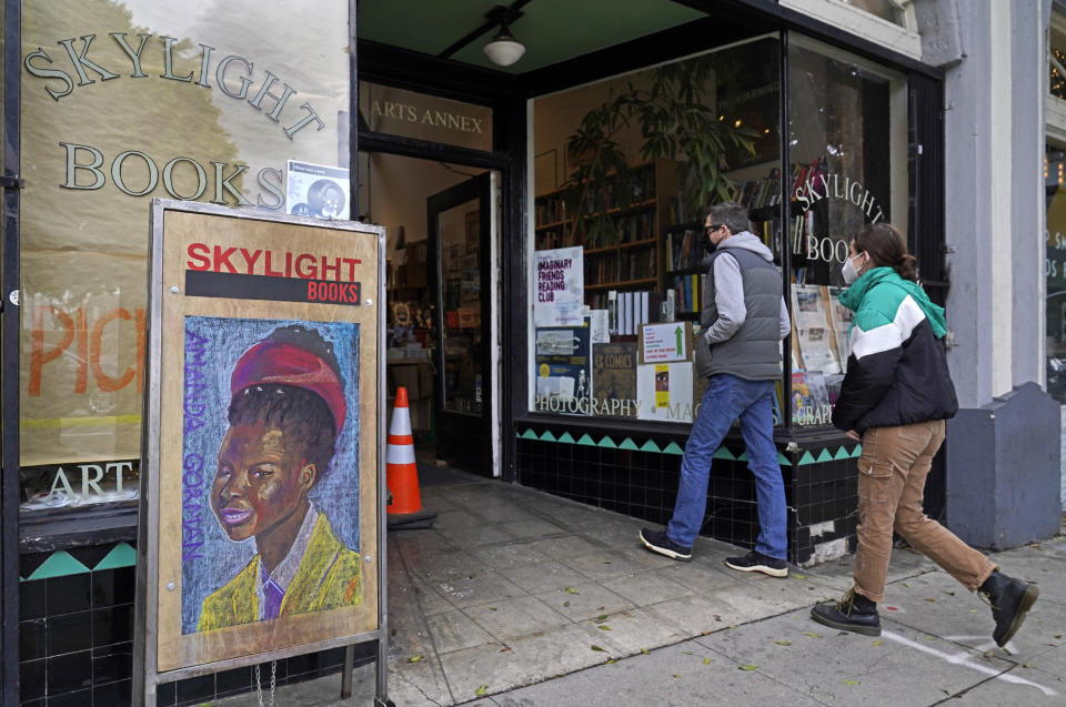 Eric y Tess de Pasadena, California, entran a la librería Skylight en Los Ángeles el 25 de enero de 2021, donde en la entrada hay una imagen de la joven poeta laureada Amanda Gorman. California ha derogado la orden regional de permanecer en casa al mejorar la situación. También deroga el toque de queda que regía desde las 10 de la noche hasta las 5 de la mañana. (AP Foto/Damian Dovarganes)