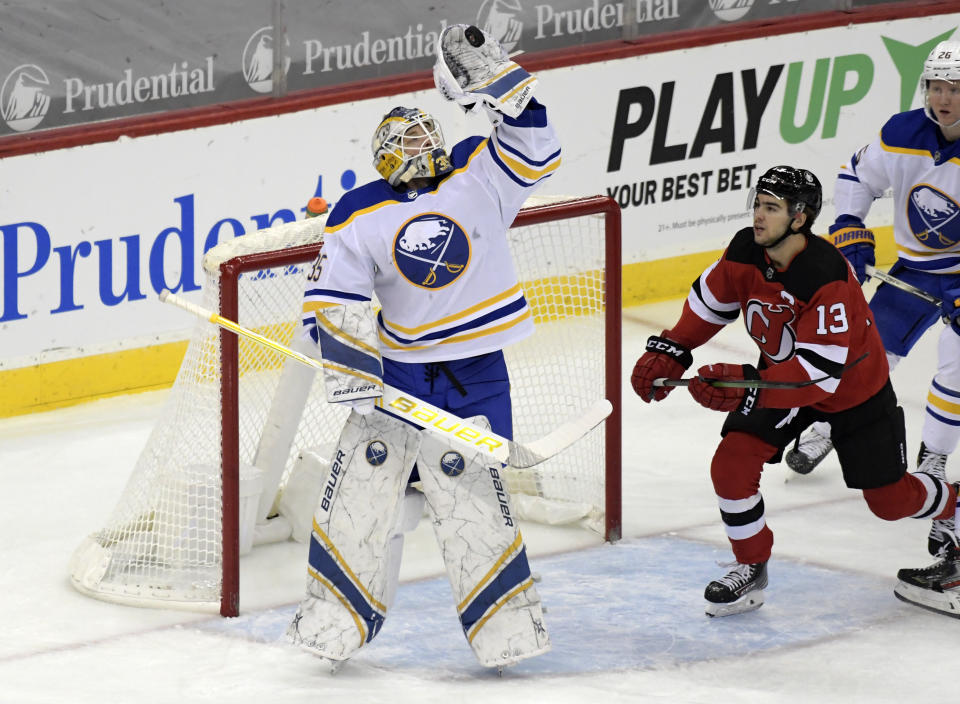 Buffalo Sabres goaltender Linus Ullmark (35) gloves the puck as New Jersey Devils center Nico Hischier (13) looks on during the first period of an NHL hockey game Tuesday, Feb. 23, 2021, in Newark, N.J. (AP Photo/Bill Kostroun)