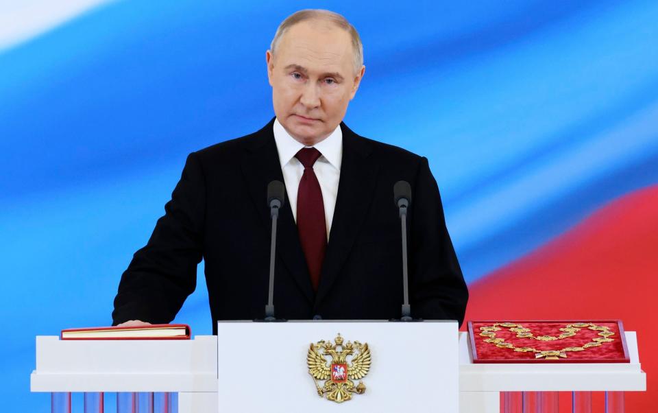 Putin places one hand on a book as he stands behind a lectern with the Russian seal on it