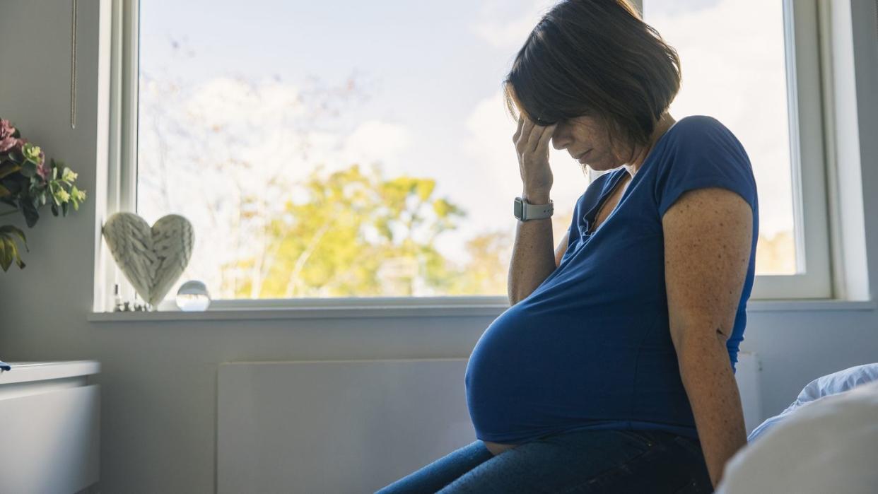 mature pregnant woman sitting on her bed negative emotion