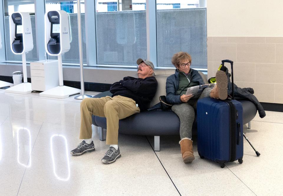 Lynne Jones reads while her husband, Chuck, sleeps after their flight to Chicago was delayed at John Glenn Columbus International Airport. The pair, from Cambridge, expect to fly there later this evening to visit their son for the holiday weekend.