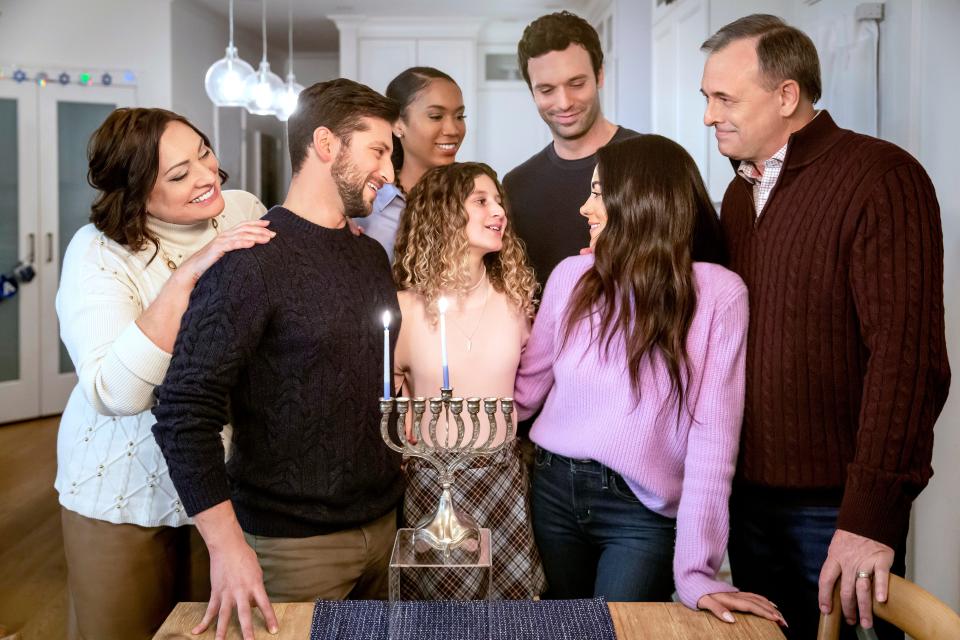 A scene from Hallmark's Hanukkah movie "Eight Gifts of Hanukkah." A family gathers around a lit menorah.
