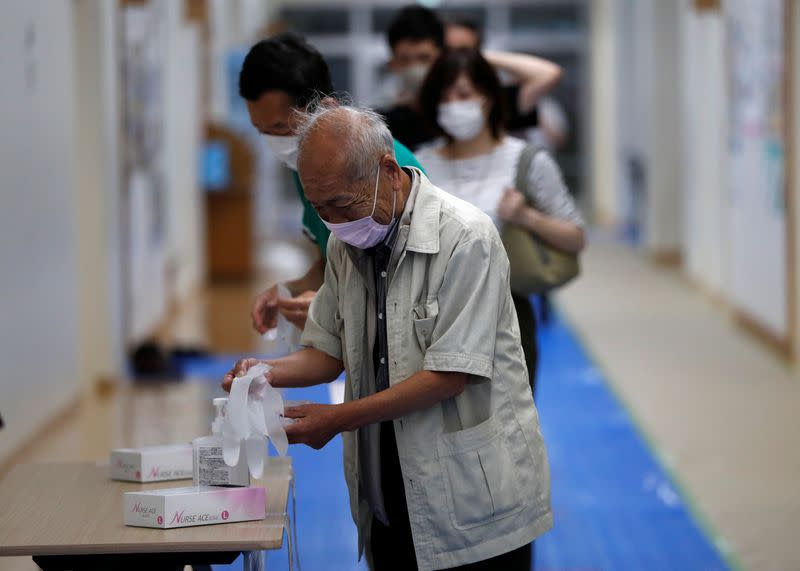 Voters wearing protective face masks disinfect their hands and put on vinyl gloves at the entrance of a voting station for the Tokyo Governor election amid the coronavirus disease (COVID-19) outbreak, in Tokyo
