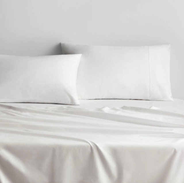 A bed made up in white linen and white pillows sits against a white wall.